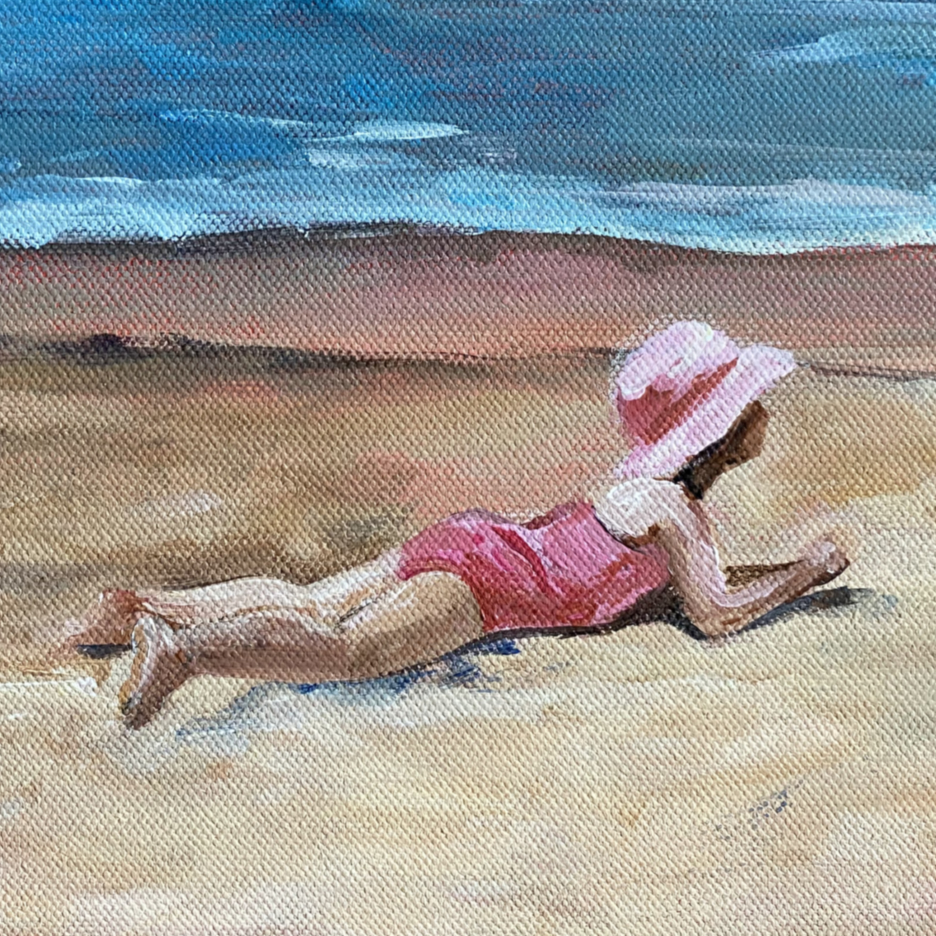 A young girl is lying on the sand. She is wearing a pink bathing suit and a pink hat. Behind her is a seashore with waves, while further in the background are some cliffs.