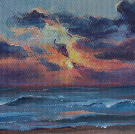 Sun is rising over a beach in Mexico. There are gently lapping waves and clouds that are silhouetted in dark blues and purples as the sun appears behind them.