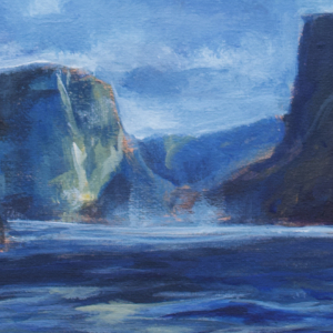 From the water's perspective, large blue cliffs frame a lightly cloudy blue sky.
